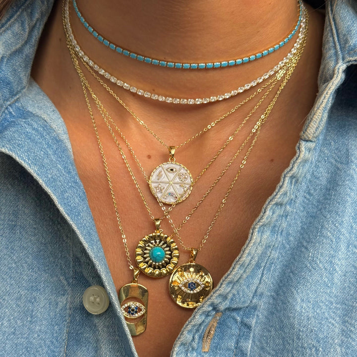 Close-up of layered necklaces with pendants on a person wearing a denim shirt.