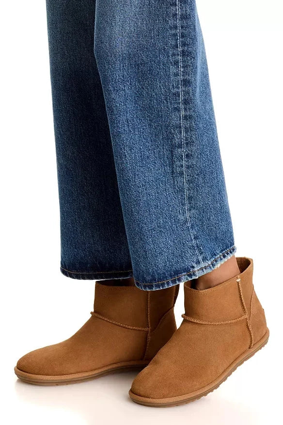 A person wearing brown suede ankle boots with blue jeans, shown from the calves down against a clean white background.