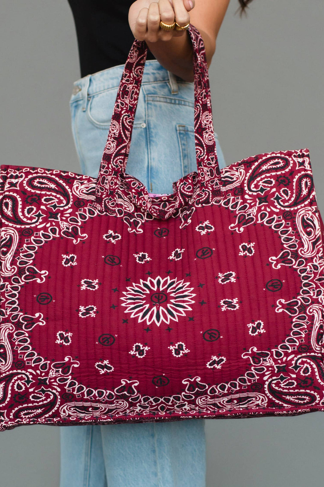 A person holding a large quilted tote bag with a red paisley bandana pattern, shown against a plain gray studio background.