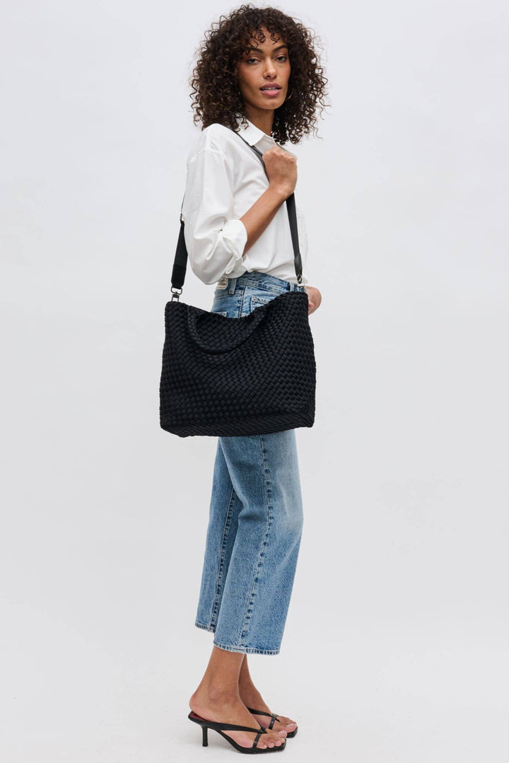 Woman holding a black woven handbag against a white background