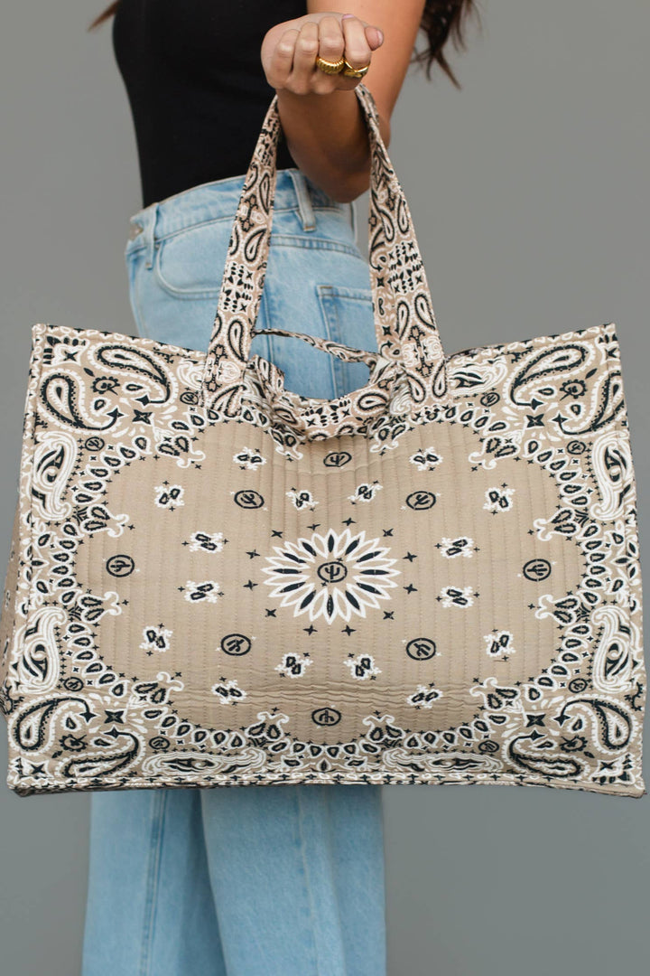 Person holding a large tote bag with bandana pattern against a gray background