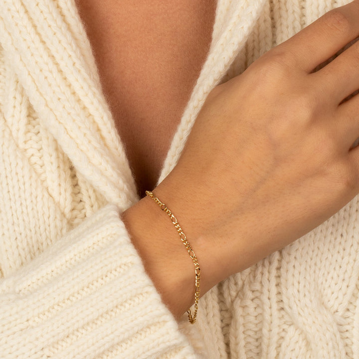 Gold bracelet on a wrist with a white knit sweater