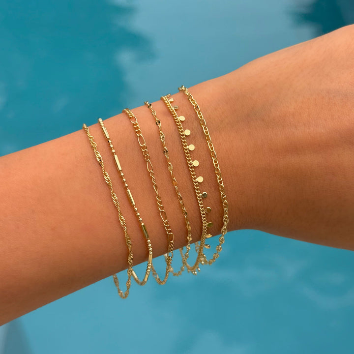 Gold bracelets on a wrist with a blue water background