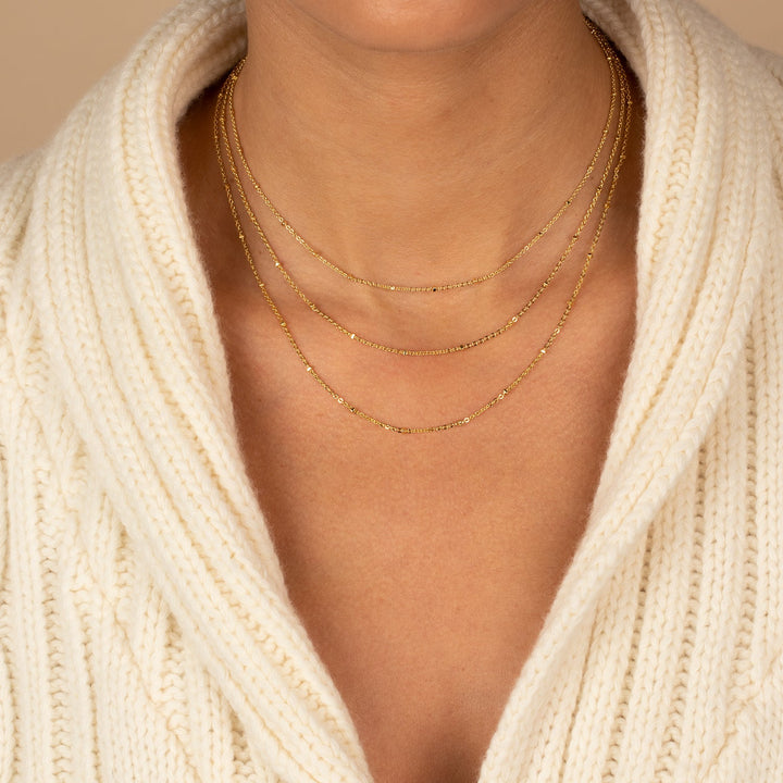 Close-up of a person wearing gold necklaces with a beige sweater.