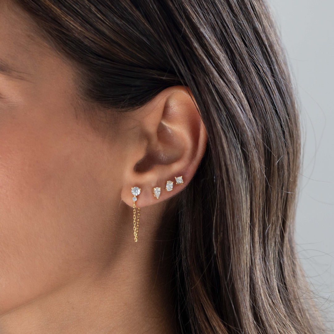 Close-up of an ear wearing gold and diamond earrings with a neutral background