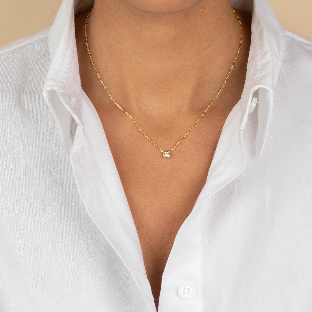 Gold necklace with a small pendant worn by a person in a white shirt.
