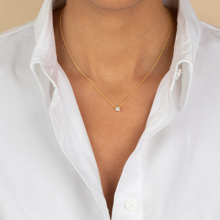 Gold necklace with a small pendant worn by a person in a white shirt.
