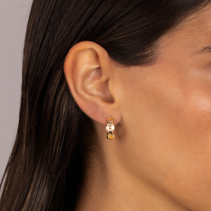 Close-up of an ear wearing a gold earring with a heart charm on a neutral background