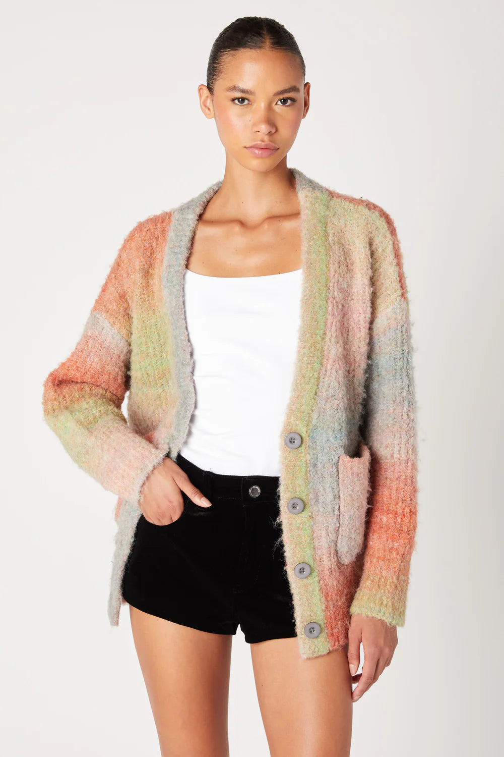 Woman wearing a colorful cardigan over a white top and black shorts on a white background