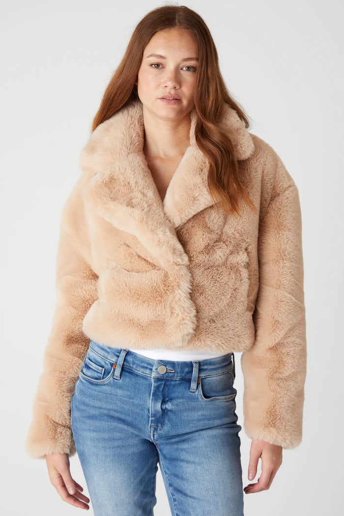Woman wearing a beige faux fur jacket and blue jeans on a white background