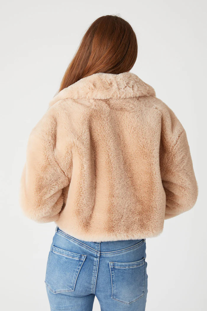 Person wearing a beige faux fur jacket and blue jeans on a white background
