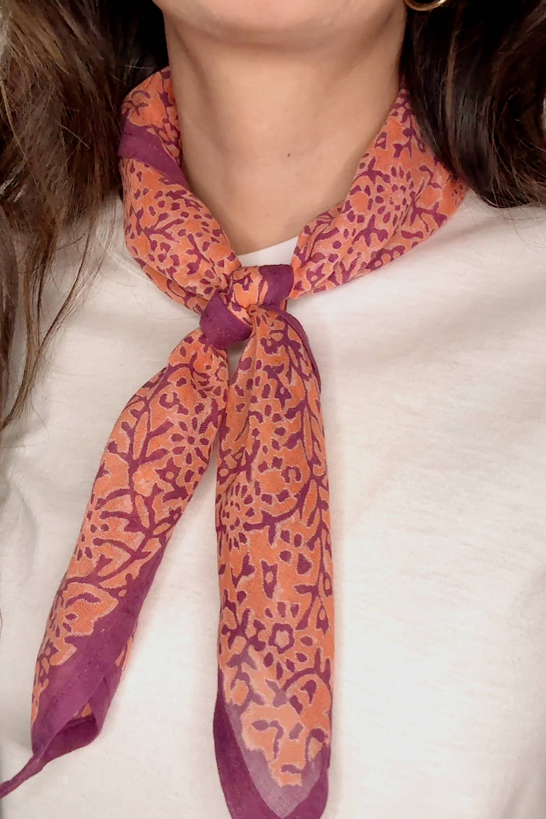 Person wearing a patterned scarf with orange and purple design on a white background