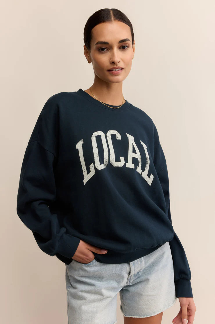 Woman wearing a navy sweatshirt with 'LOCAL' printed on it against a beige background