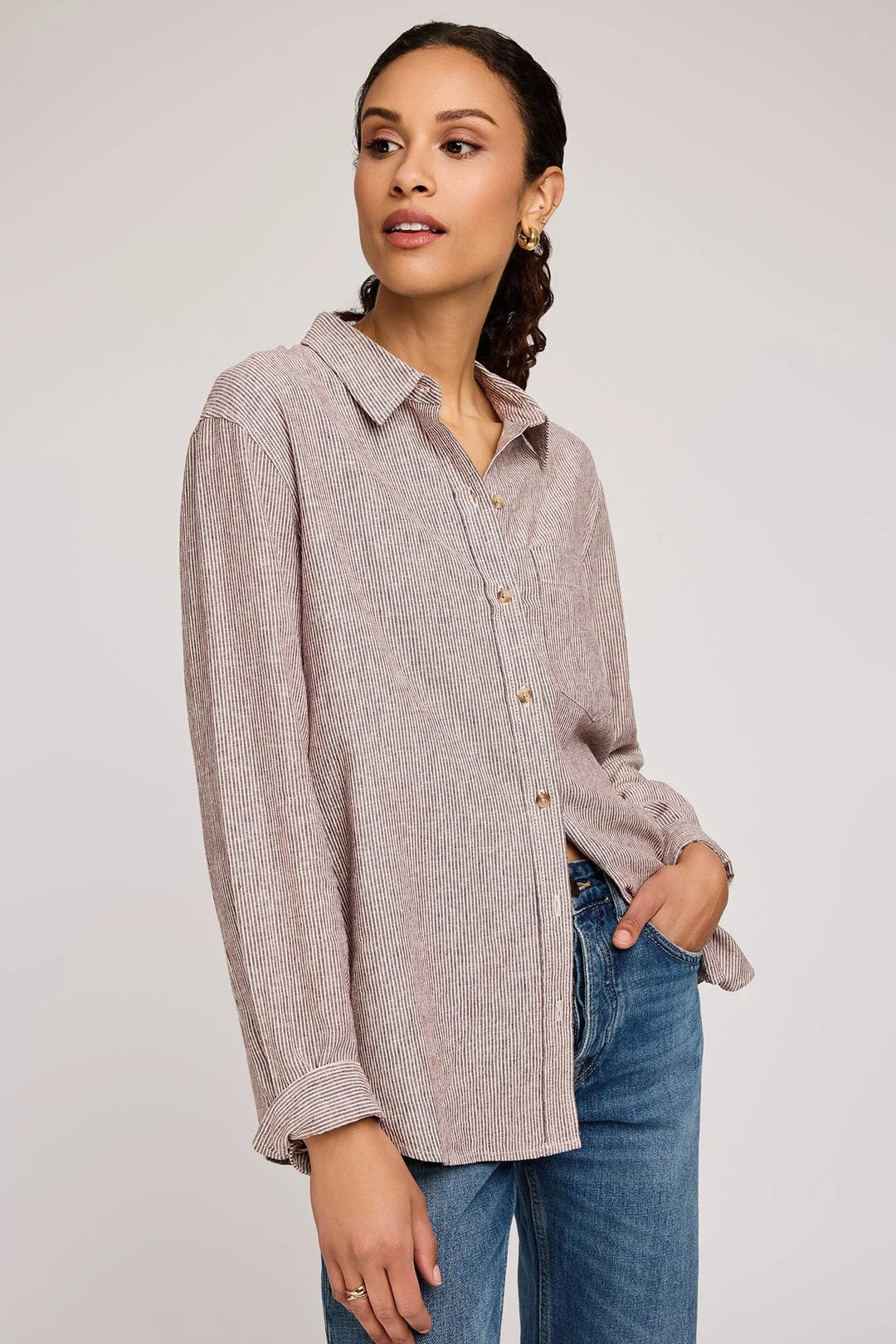 Woman wearing a light brown button-up shirt and blue jeans on a white background