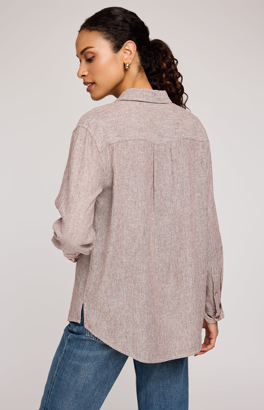 Woman wearing a beige button-up shirt and blue jeans on a plain background