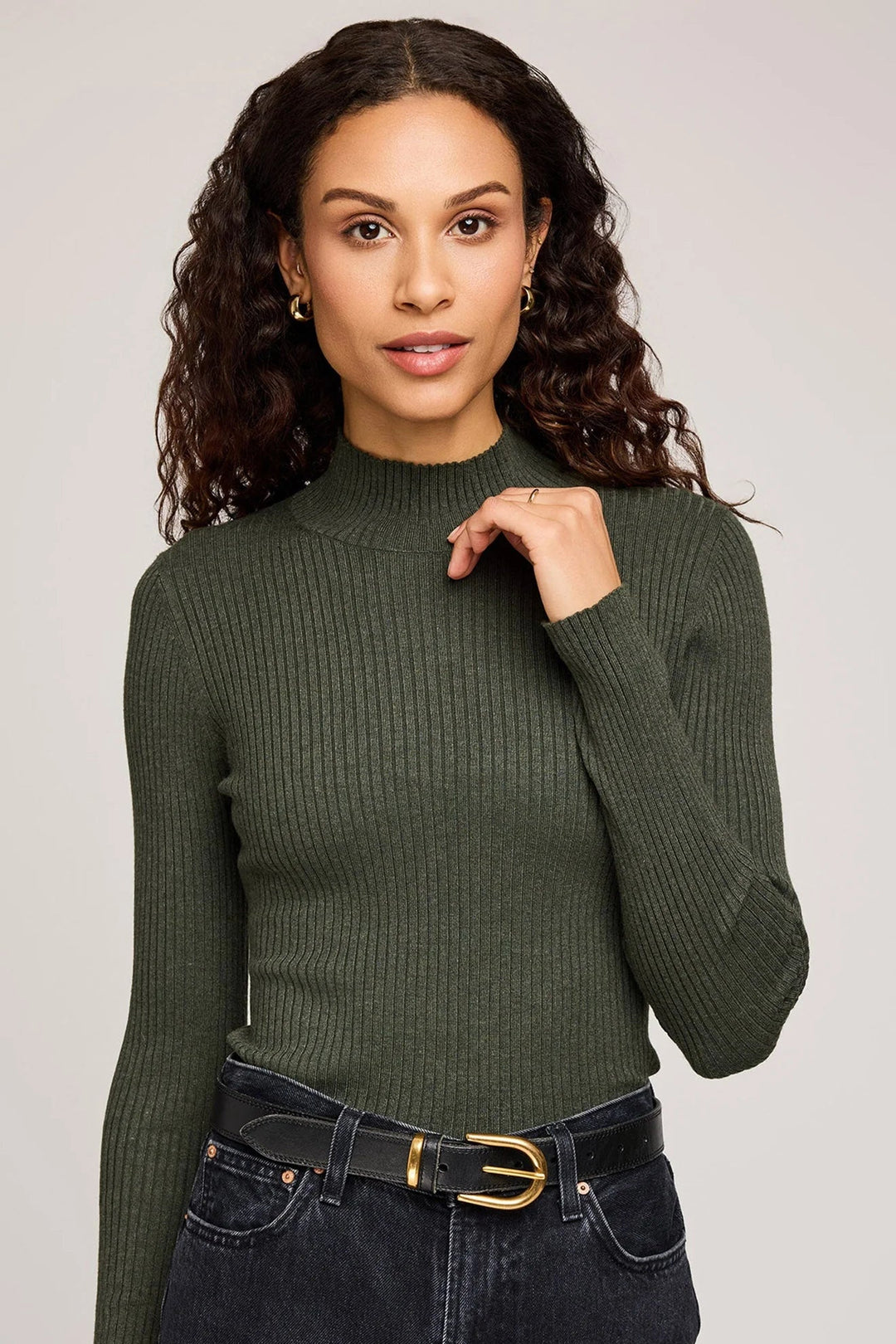 Woman wearing a green ribbed sweater and black jeans against a plain background