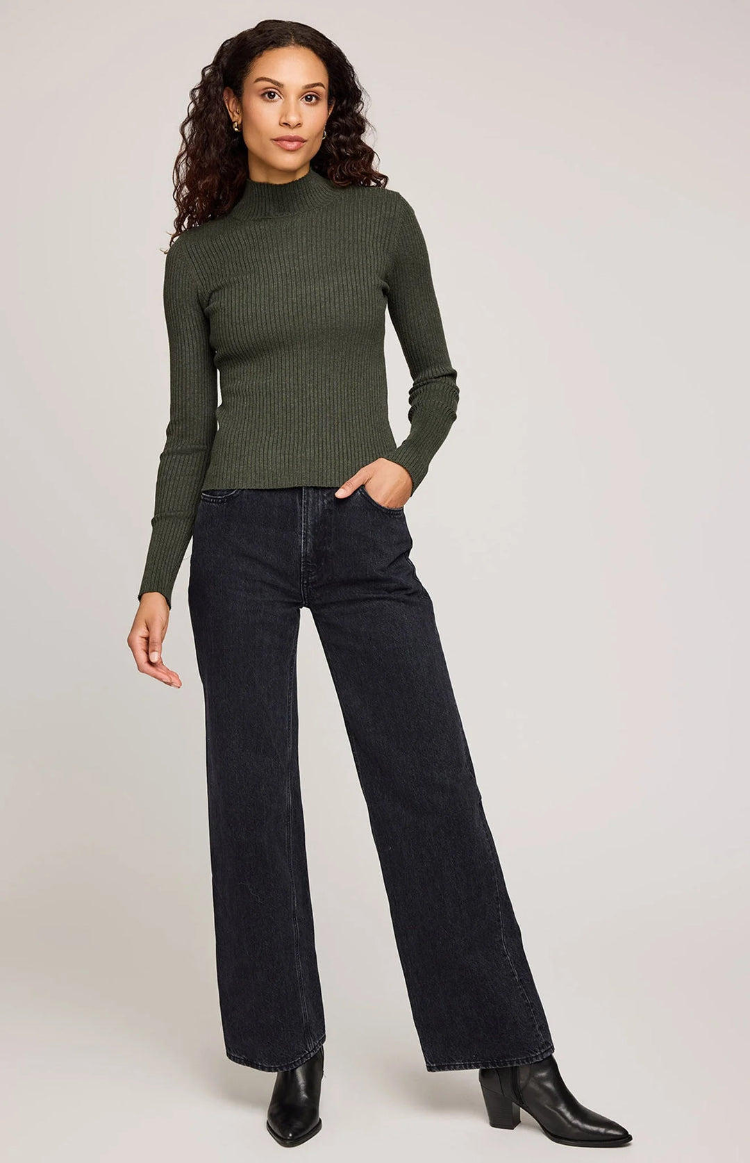 Woman wearing a green ribbed sweater and black jeans on a white background