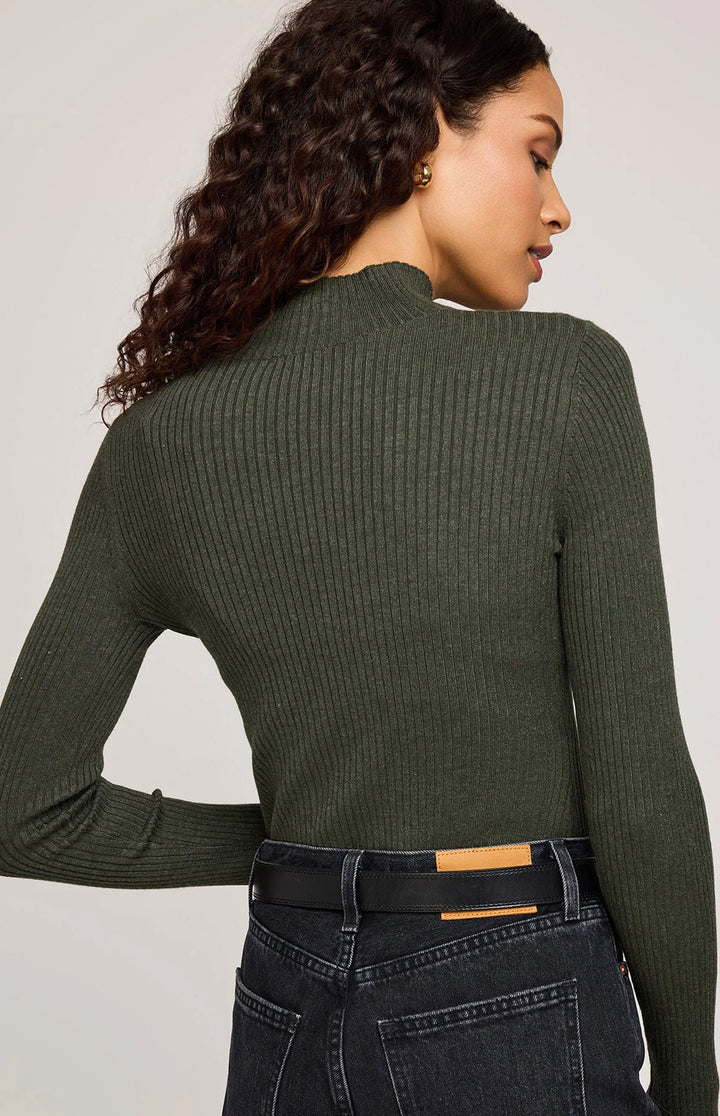 Person wearing a green ribbed sweater and dark jeans on a plain background