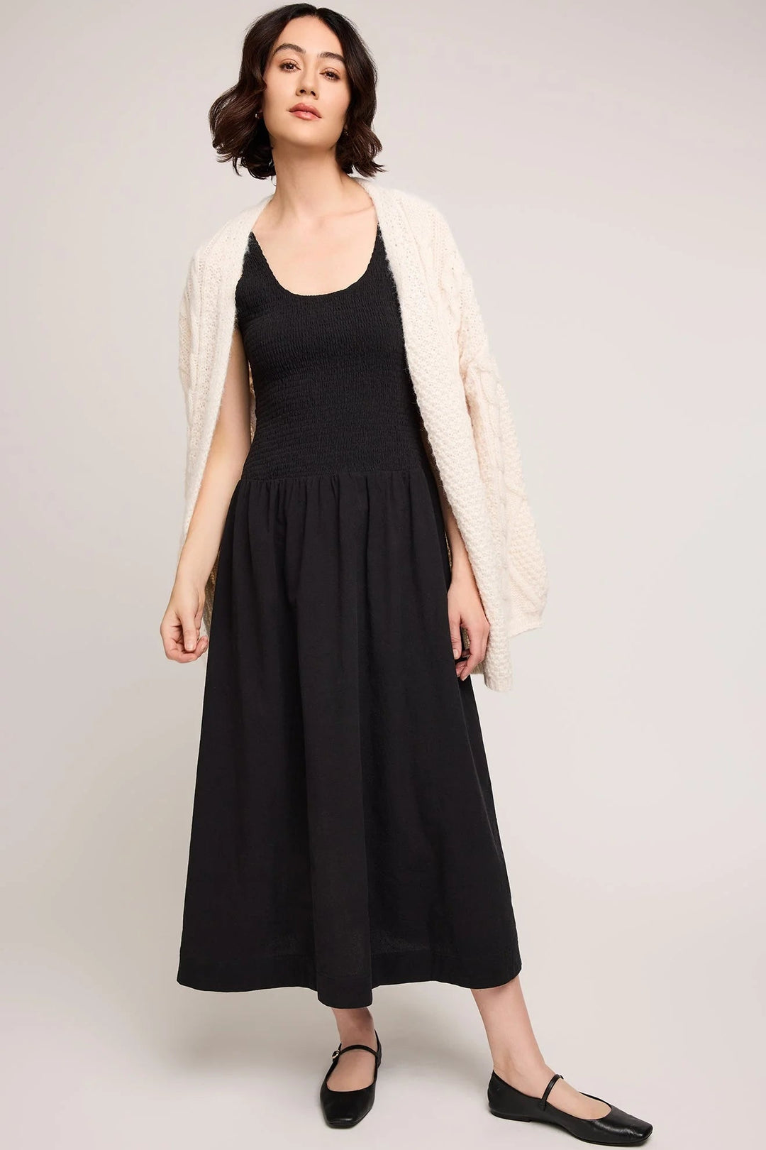 Woman wearing a black dress with a white cardigan on a plain background