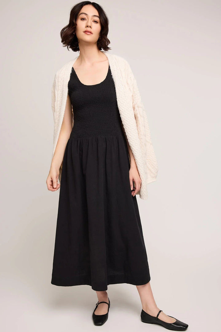 Woman wearing a black dress with a white cardigan on a plain background