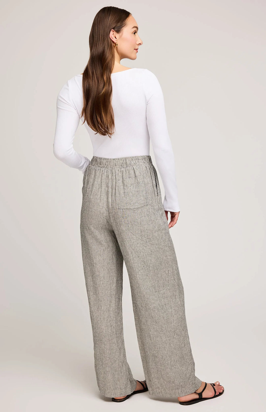 Woman wearing gray wide-leg pants and a white top on a plain background