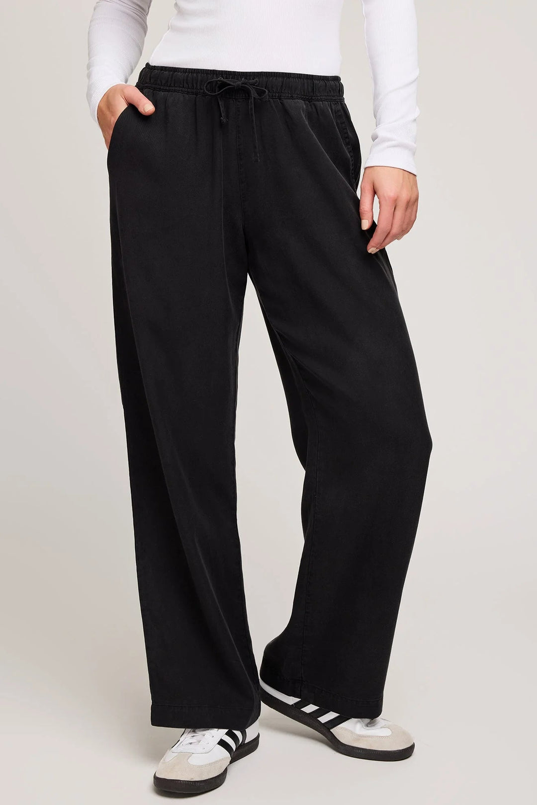 Person wearing black pants and white sneakers on a plain background
