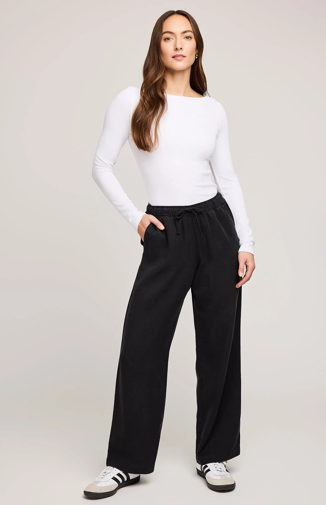 Woman wearing a white long-sleeve top and black wide-leg pants on a plain background