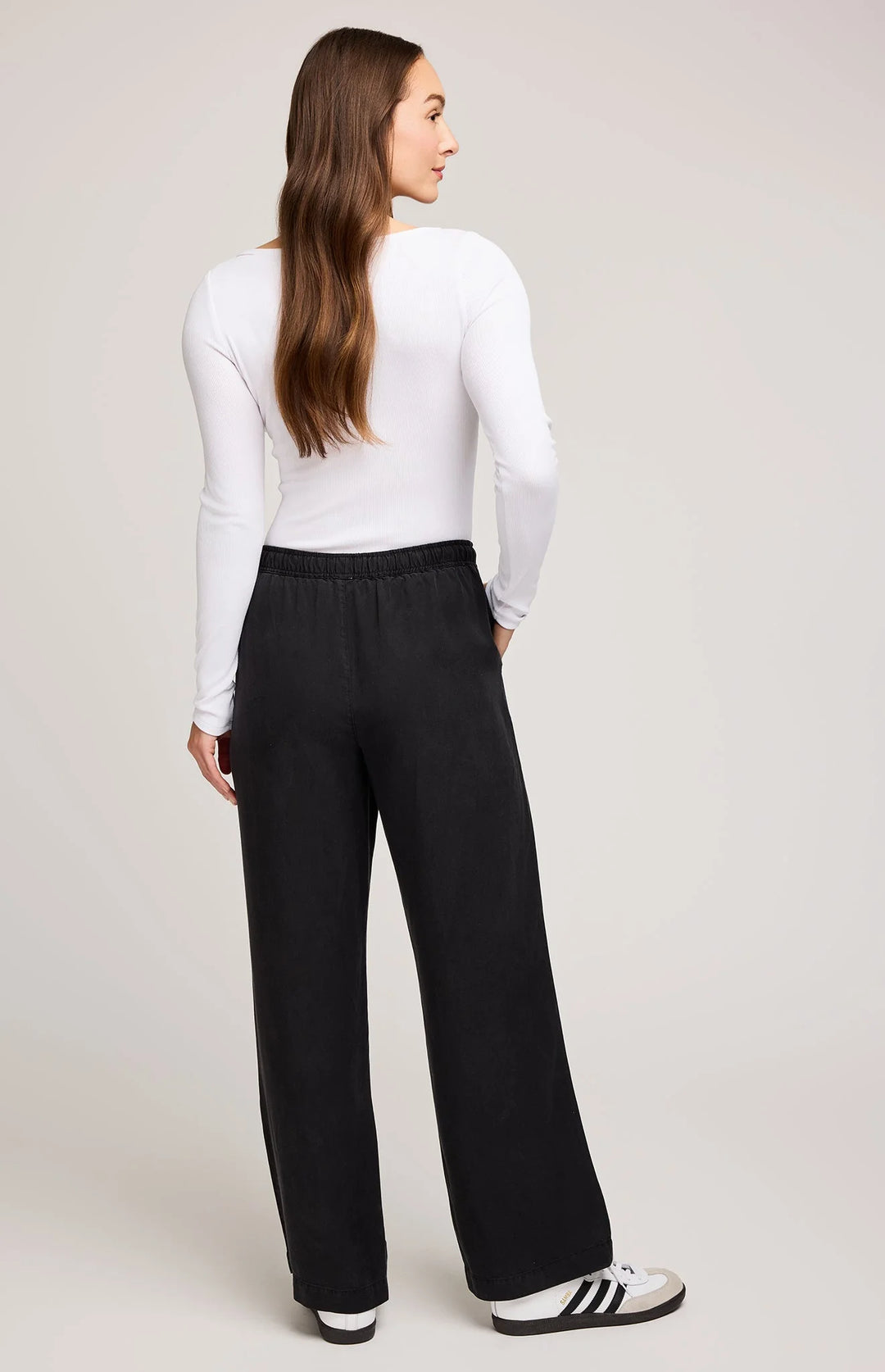 Woman wearing a white long-sleeve top and black wide-leg pants on a plain background