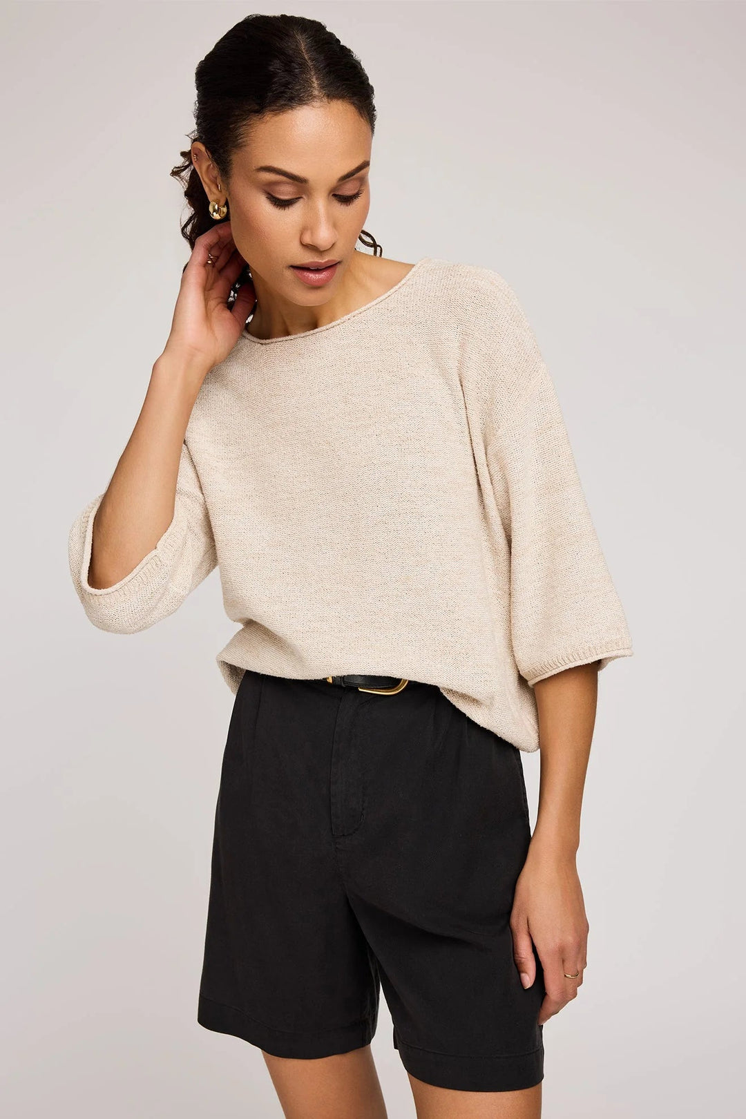 Woman wearing a beige sweater and black shorts on a plain background