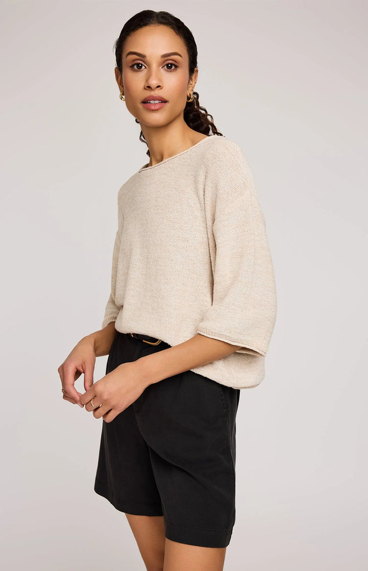 Woman wearing a beige sweater and black shorts against a plain background
