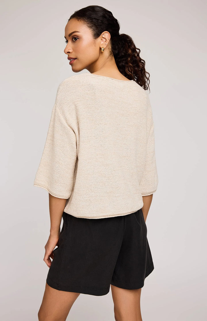 Woman wearing a beige sweater and black shorts on a plain background