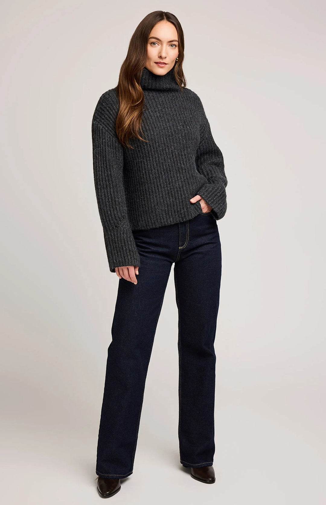 Woman wearing a dark gray ribbed sweater and black jeans on a light gray background