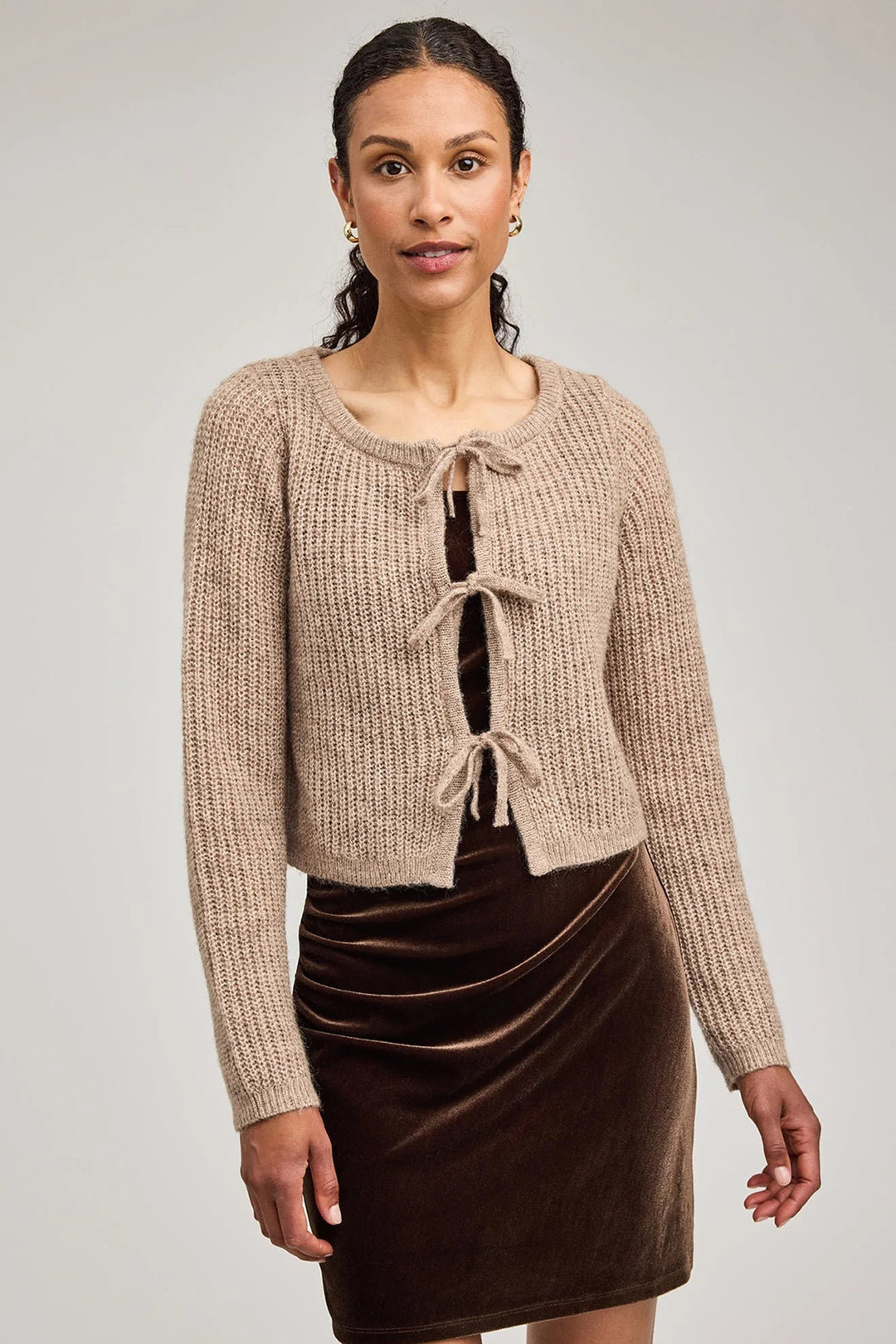 Woman wearing a beige knit cardigan over a brown dress on a plain background