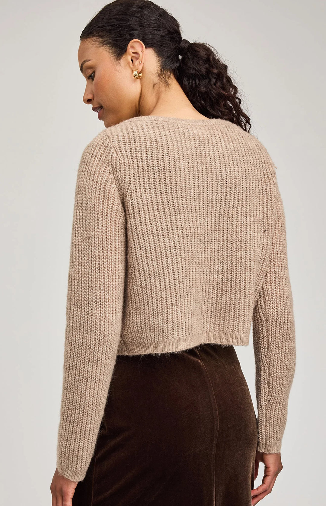Woman wearing a beige knitted sweater against a plain background
