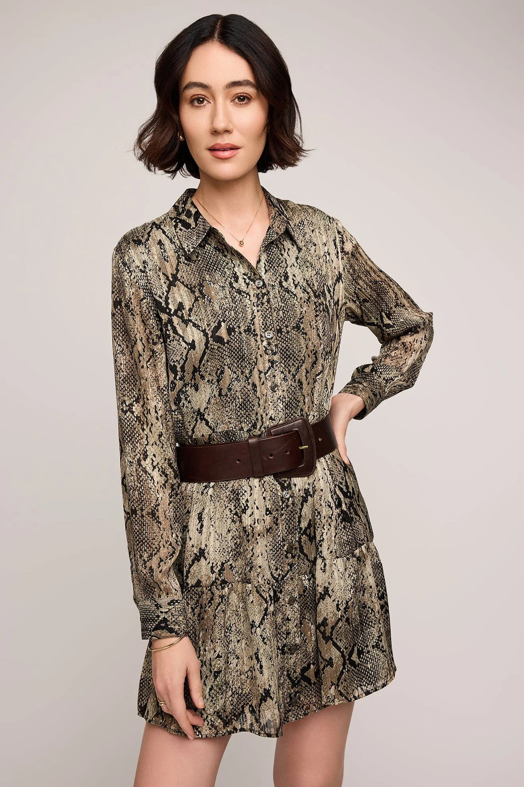 Woman wearing a snake print dress with a brown belt on a plain background