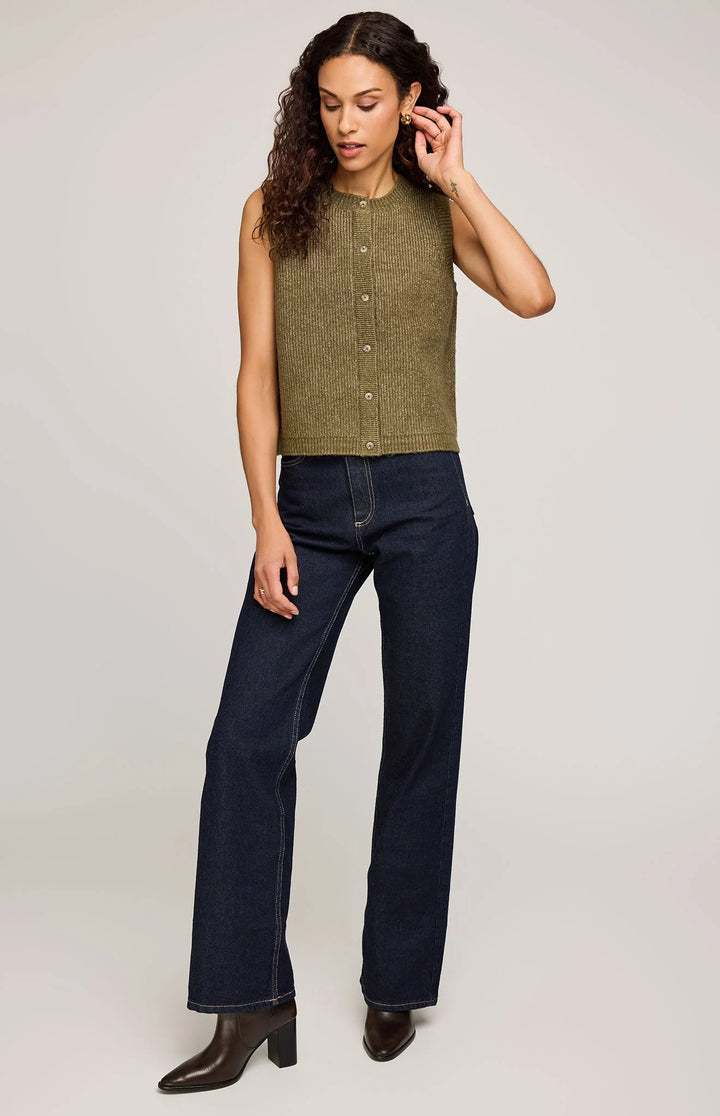 Woman wearing a green sleeveless vest top and dark blue jeans on a plain background