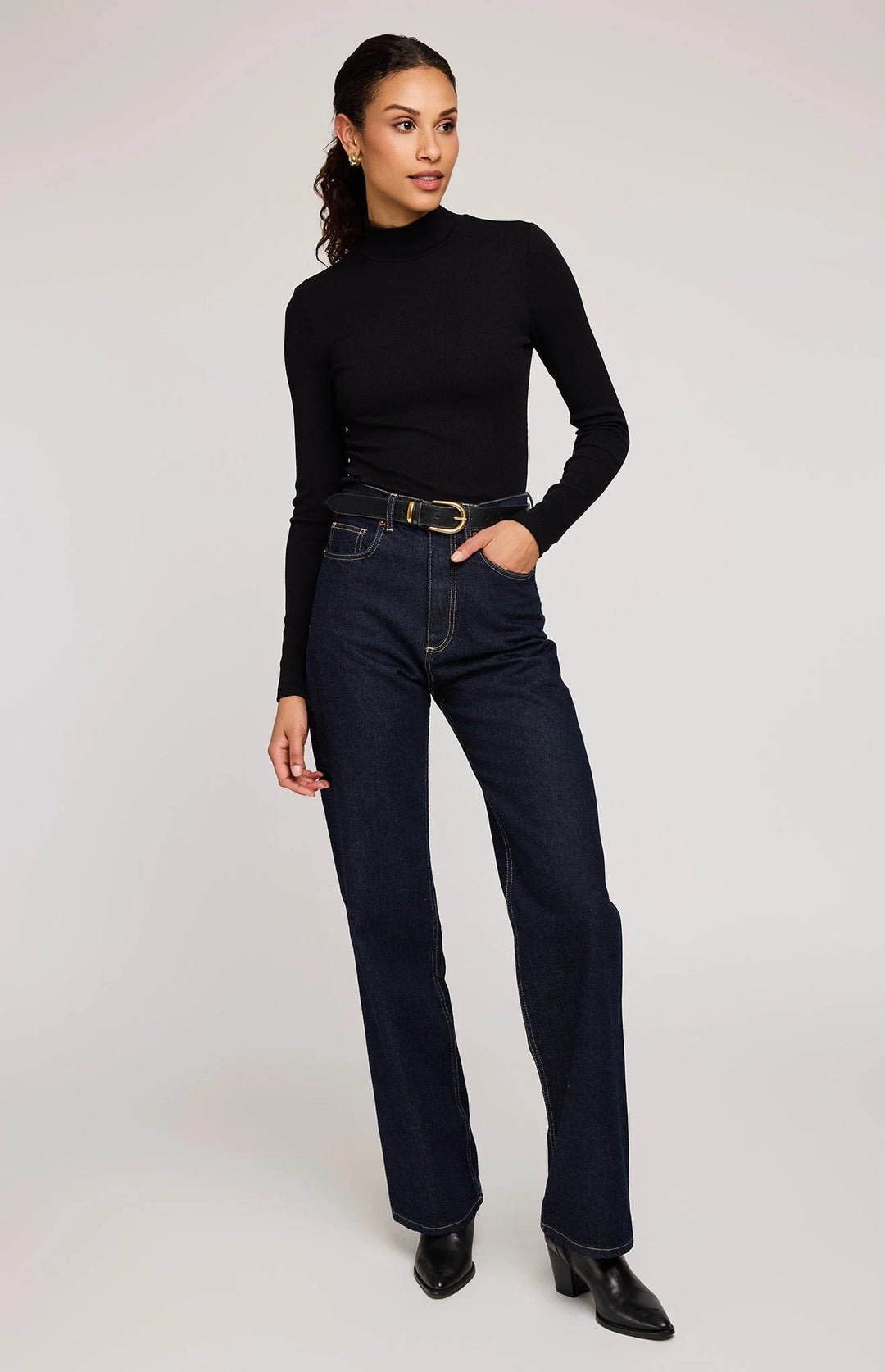 Woman wearing a black turtleneck and dark jeans on a white background