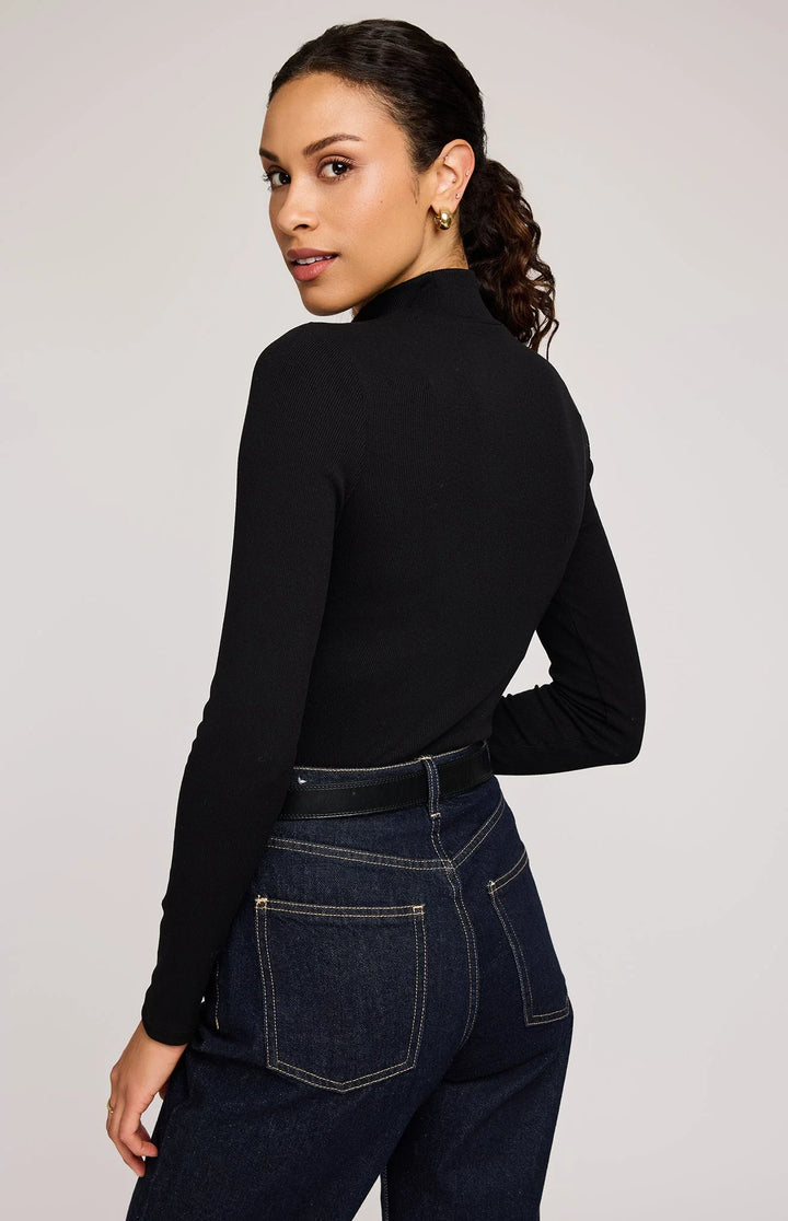 Woman wearing a black long-sleeve top and dark jeans on a plain background