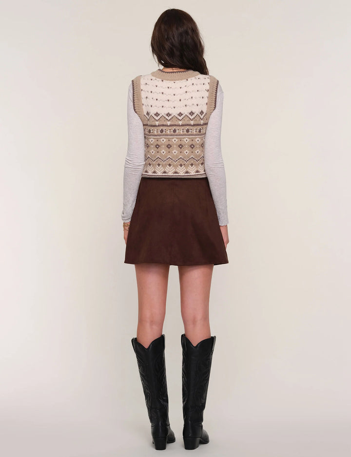 Person wearing a patterned top, brown skirt, and black boots on a plain background