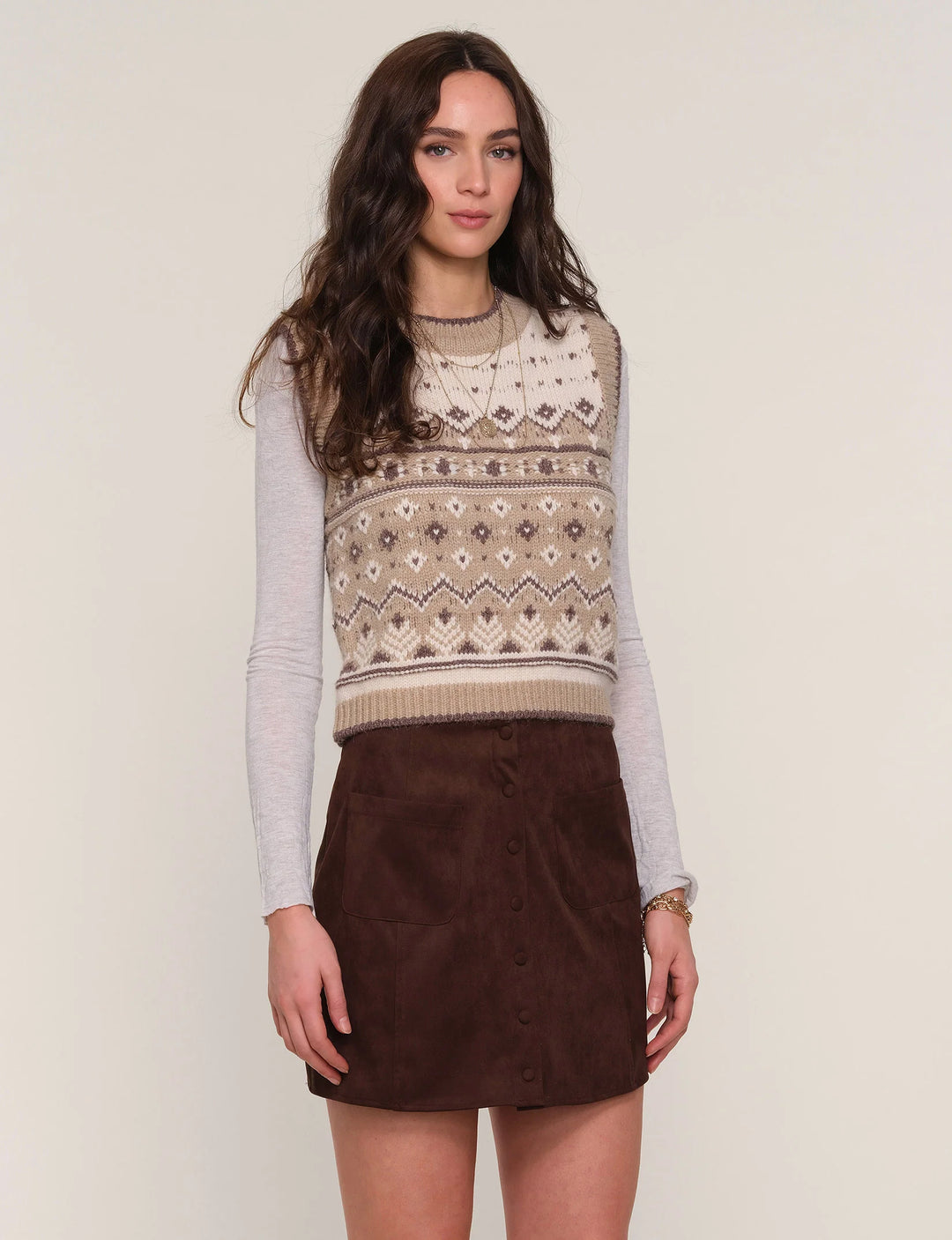 Woman wearing a patterned sweater vest and brown skirt on a plain background