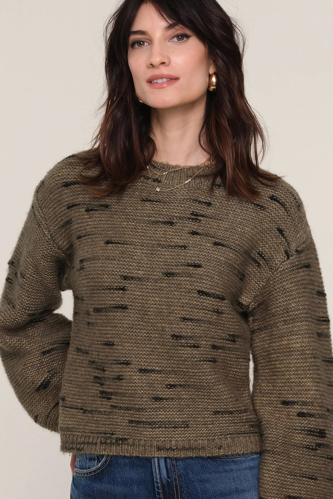 Woman wearing a brown knitted sweater with black speckles on a plain background