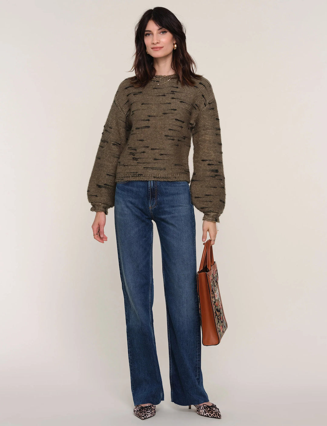 Woman wearing a patterned sweater and blue jeans, holding a brown bag on a white background