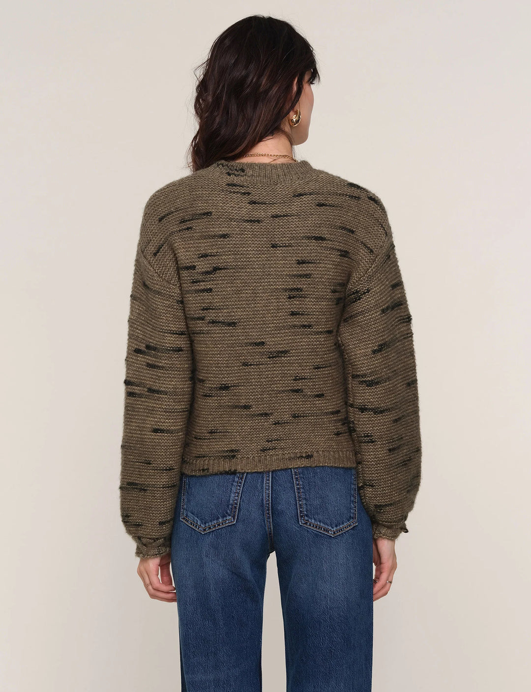 Person wearing a green patterned sweater and blue jeans on a beige background