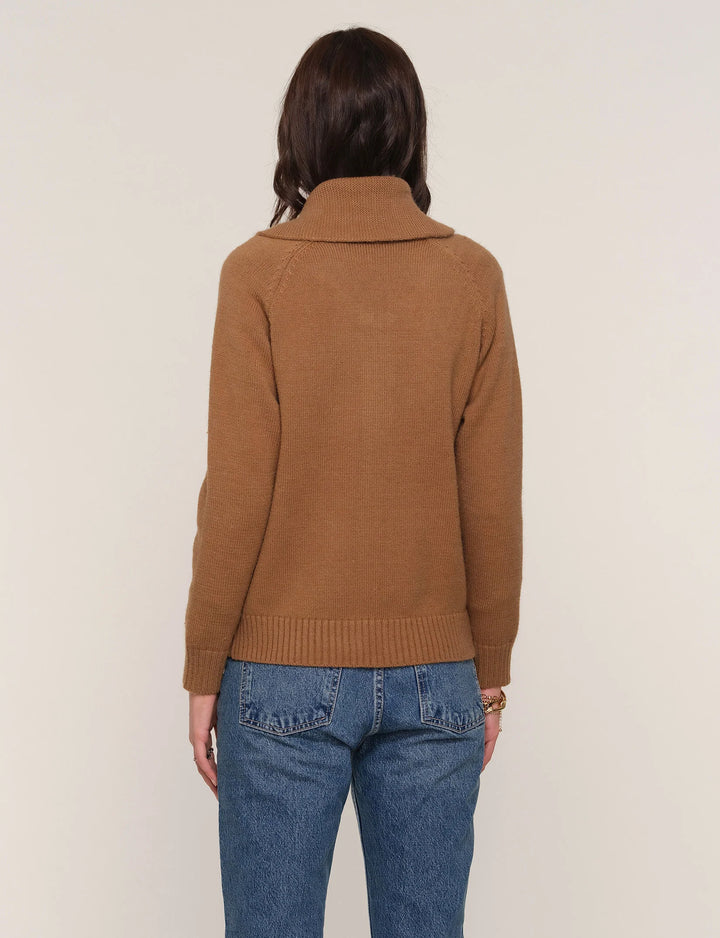 Person wearing a brown sweater and blue jeans against a plain background