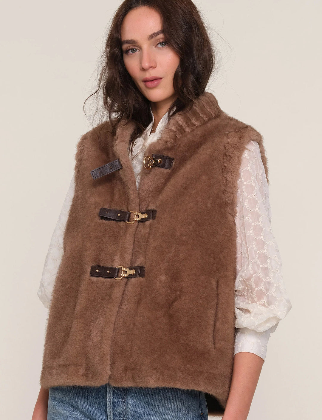 Woman wearing a brown vest over a white shirt on a beige background