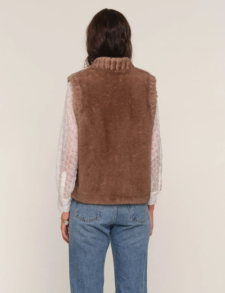 Person wearing a brown vest over a sheer top and jeans on a plain background