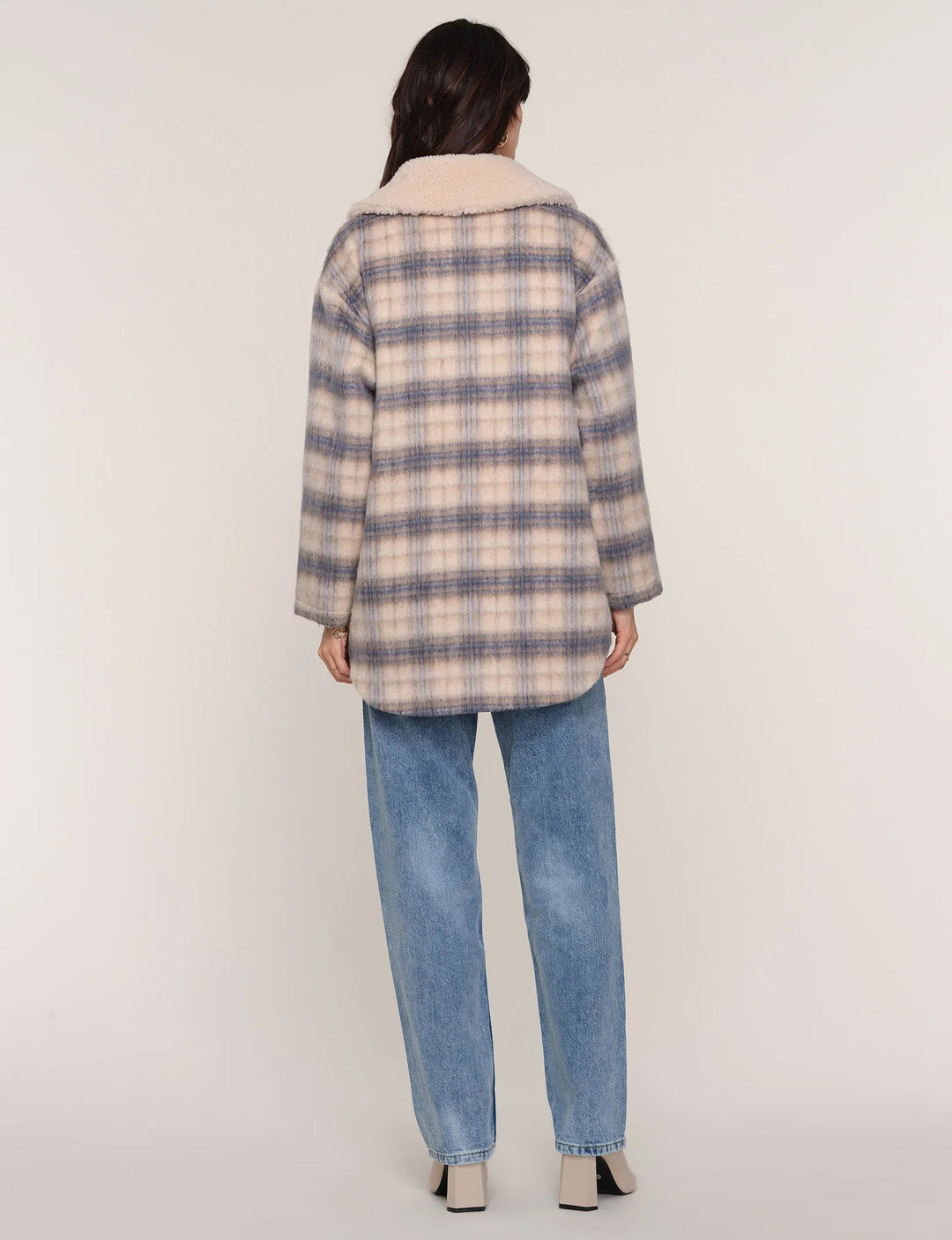 Person wearing a plaid coat and jeans on a white background