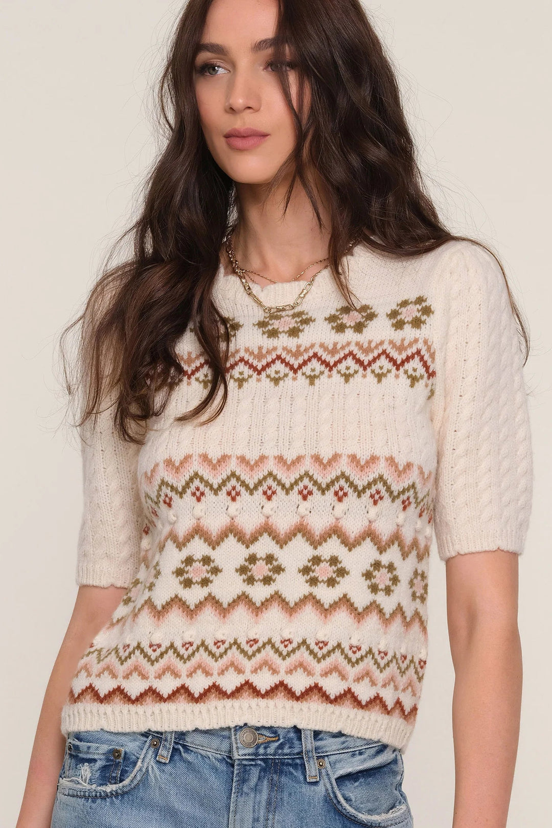 Woman wearing a patterned sweater and jeans on a plain background
