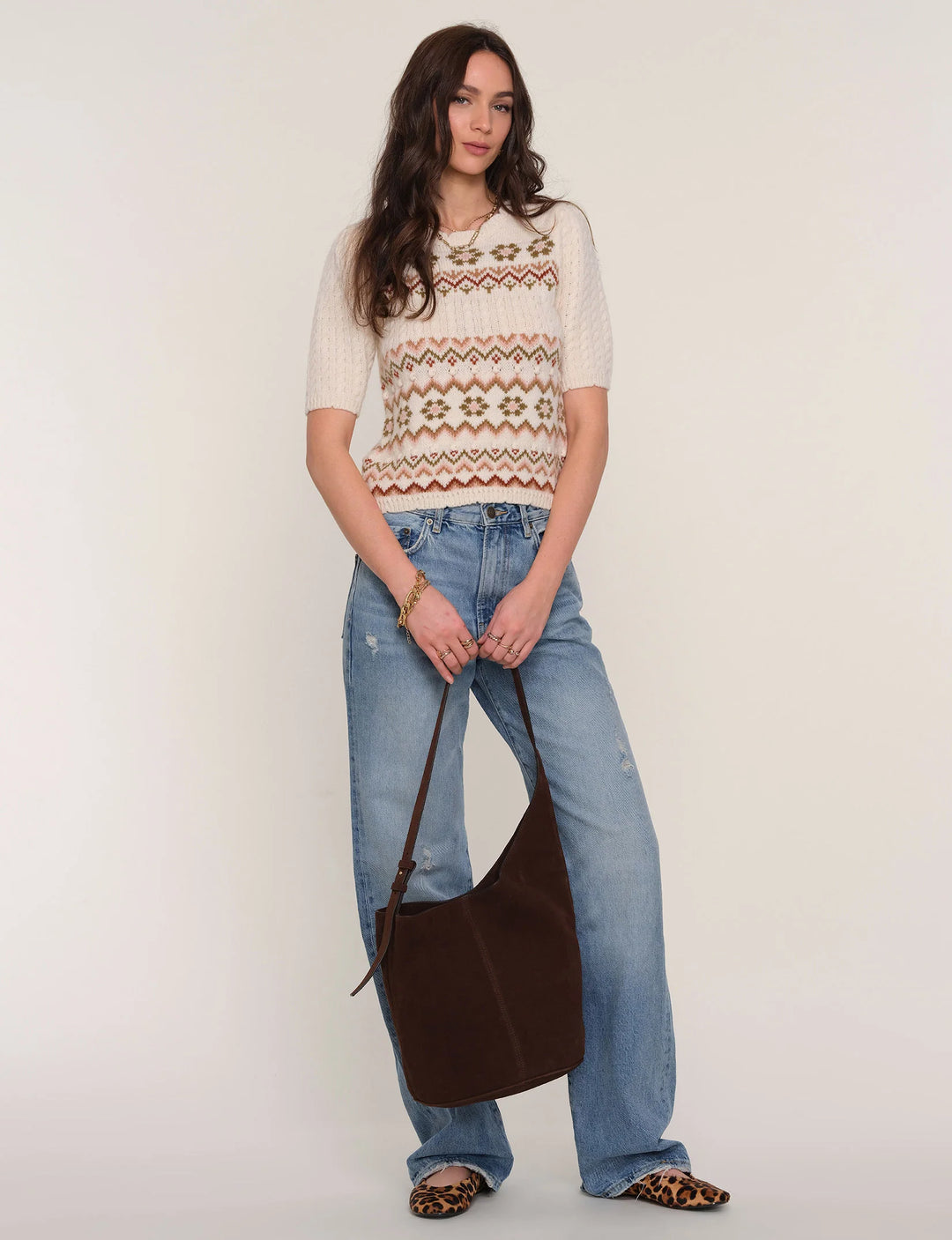 Woman wearing a patterned sweater and jeans, holding a brown bag on a white background