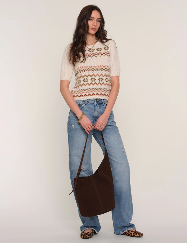 Woman wearing a patterned sweater and jeans, holding a brown bag on a white background